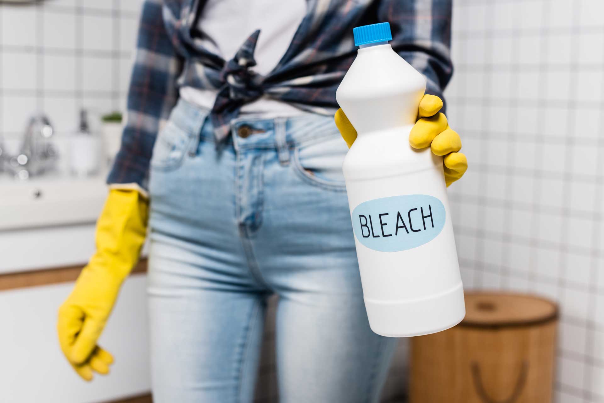 Lady holding bleach bottle with yellow plastic gloves